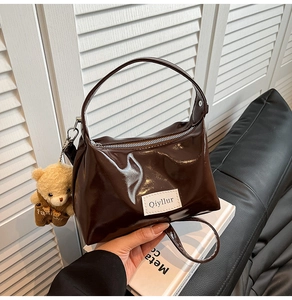 Close-up of brown patent leather tote bag with a cute teddy bear plush charm