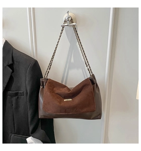 Detail of suede patchwork and gold metal logo plate on brown leather chain tote bag