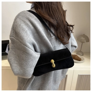 Détail du sac bandoulière en daim noir avec fermoir doré porté par un mannequin en décor