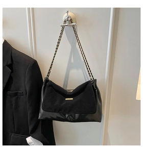 Close-up of black suede and leather patchwork tote bag with gold chain strap on blazer