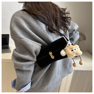 Detail of black suede shoulder bag with gold twist lock and a quirky plush monster charm