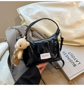 Detail of black glossy crescent bag featuring a teddy bear charm and Qiyllur label