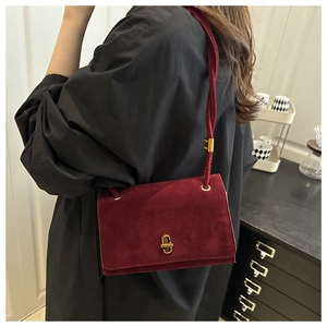 Close-up of a burgundy suede clutch bag with a minimalist gold metal twist lock buckle