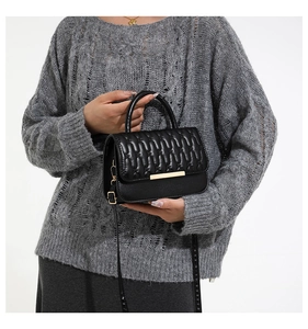 Detail of a black quilted handbag featuring a gold metal clasp and top handle held by a model