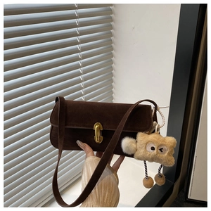 Dettaglio borsa sottobraccio in camoscio marrone scuro con fibbia dorata e ciondolo di peluche
