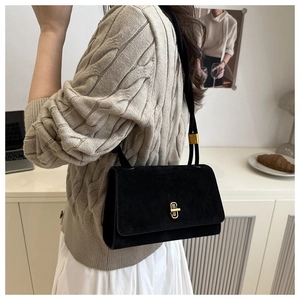 Detail of elegant black suede handbag with gold turn-lock worn by a model in soft lighting