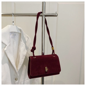 Detail of burgundy suede shoulder bag featuring a knotted strap and gold twist-lock closure