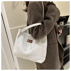 Detail of white corduroy tote bag with brown leather logo patch on a shoulder strap