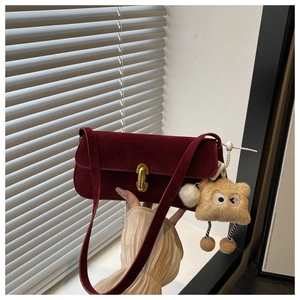 Dettaglio borsa a spalla in camoscio bordeaux con chiusura dorata e ciondolo peluche