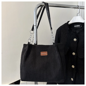 Detail of black corduroy tote bag showing leather label and silver metal chain strap