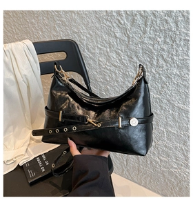 Close-up of black glossy crescent bag with golden hardware and buckle strap detail