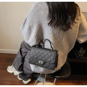 Close-up of black quilted crossbody bag with metal lock worn by a model in warm light