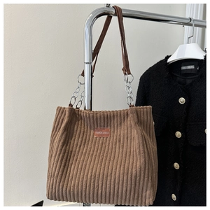 Close-up of brown corduroy tote bag featuring a leather logo patch and metal chain strap