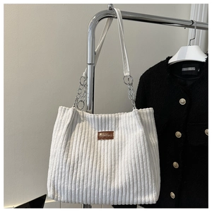 Close-up of white corduroy tote bag with brown leather tag and metal chain strap