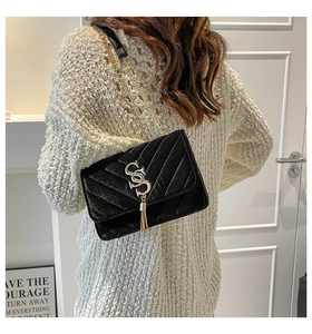 Detail of black quilted shoulder bag with gold SS logo and tassel on white sweater