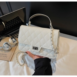White quilted crossbody bag with silver lock shown with a laptop and books on a desk