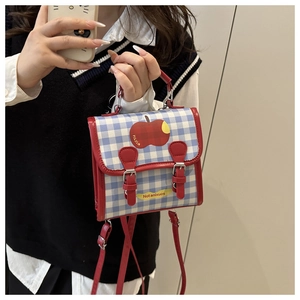 Detail of blue plaid mini bag with red apple print and decorative buckle straps