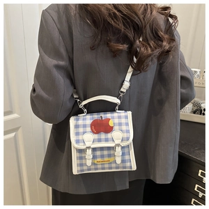 Detail of blue and white checkered crossbody bag featuring a red apple and a leather label