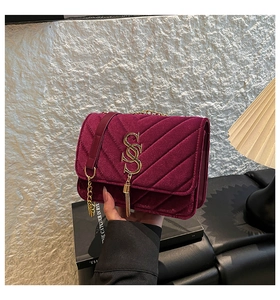 Close-up of burgundy velvet crossbody bag with V-quilting, gold chain, and fringe detail
