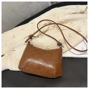 Detail of a brown leather crossbody bag with knot design on a knitted sweater