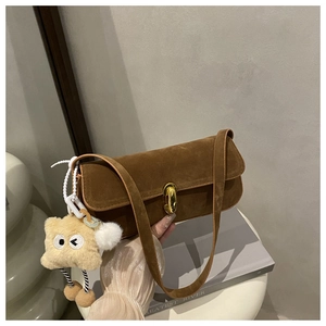 Close-up of brown suede underarm bag with gold metal lock and a cute plush charm