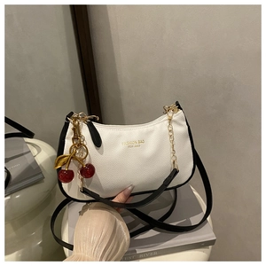 Detail of white lychee leather handbag with black trim, gold chain, and cherry charm