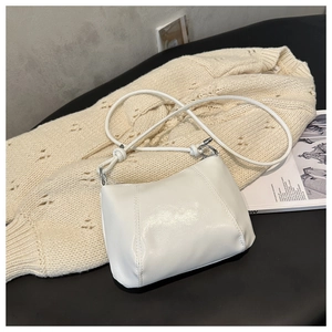 Detail of white hobo bag with knotted strap on beige knit sweater and magazine