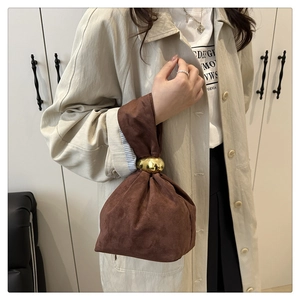Detail of dark brown suede bucket bag featuring elegant gold metal hardware and pleats