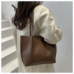 Detail shot of a dark brown textured leather tote bag worn by a model on white stairs