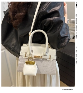 Detail showing white crocodile pattern leather handbag with gold hardware and mini charm