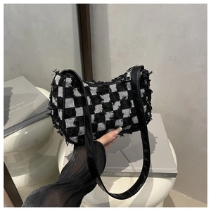 Detail of checkered pattern shoulder bag featuring frayed fringe edges and black strap