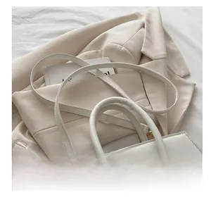 Detail of luxury white crocodile pattern handbag with gold hardware on a beige blazer