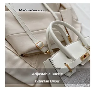 Close-up of white faux crocodile leather handbag with golden turn-lock and adjustable buckle