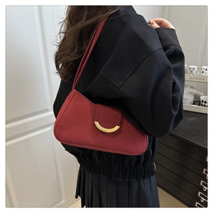 Side view of a dark red suede crescent bag with gold metal buckle on a shoulder strap