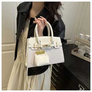 Close-up of white crocodile pattern handbag featuring gold metallic twist-lock and charm