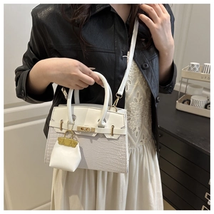 Detail of white crocodile texture handbag with gold hardware worn by a model