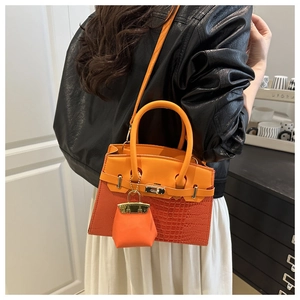 Detail of orange crocodile texture handbag with gold twist lock and mini bag charm