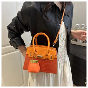 Detail of orange handbag showing crocodile pattern texture and metal turn-lock closure