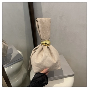 Minimalist beige suede bucket bag featuring a large decorative gold teardrop metal buckle