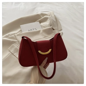 Close-up of burgundy suede shoulder bag featuring a golden crescent metal buckle