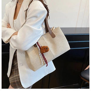 Detail of linen tote bag featuring brown leather straps and cute plush bear charm decoration