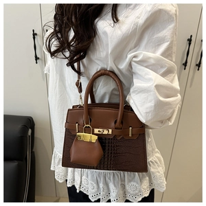 Close-up of brown crocodile texture leather bag with golden metal lock and mini charm