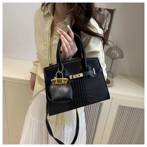 Detail of black crocodile texture handbag with golden clasp and mini bag charm