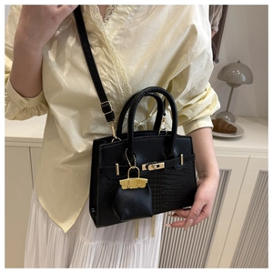 Detail of black crocodile texture handbag with gold twist lock and mini charm on strap