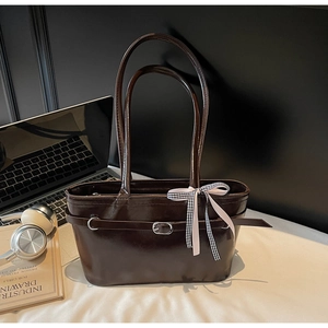 Détail du sac cabas brillant marron foncé avec nœud et accessoires de bureau professionnels