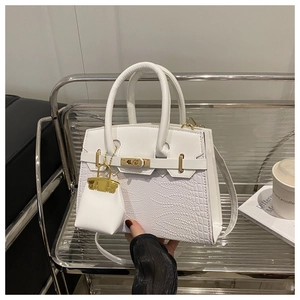 Detail of white crocodile texture leather handbag with golden twist lock and mini charm