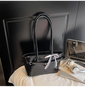Détail du sac à bandoulière noir brillant avec boucle en métal et nœud à carreaux