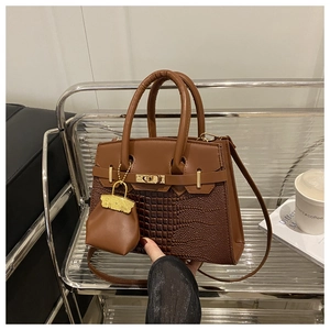 Detail of a brown croc-embossed leather handbag with gold twist lock in a modern office set
