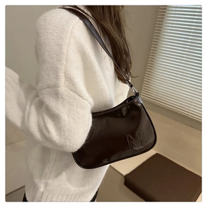 Detailed texture of dark brown patent leather shoulder bag with embossed M logo