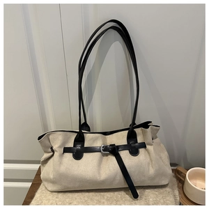 Detail of off-white suede tote bag with black leather strap on a knitted sweater